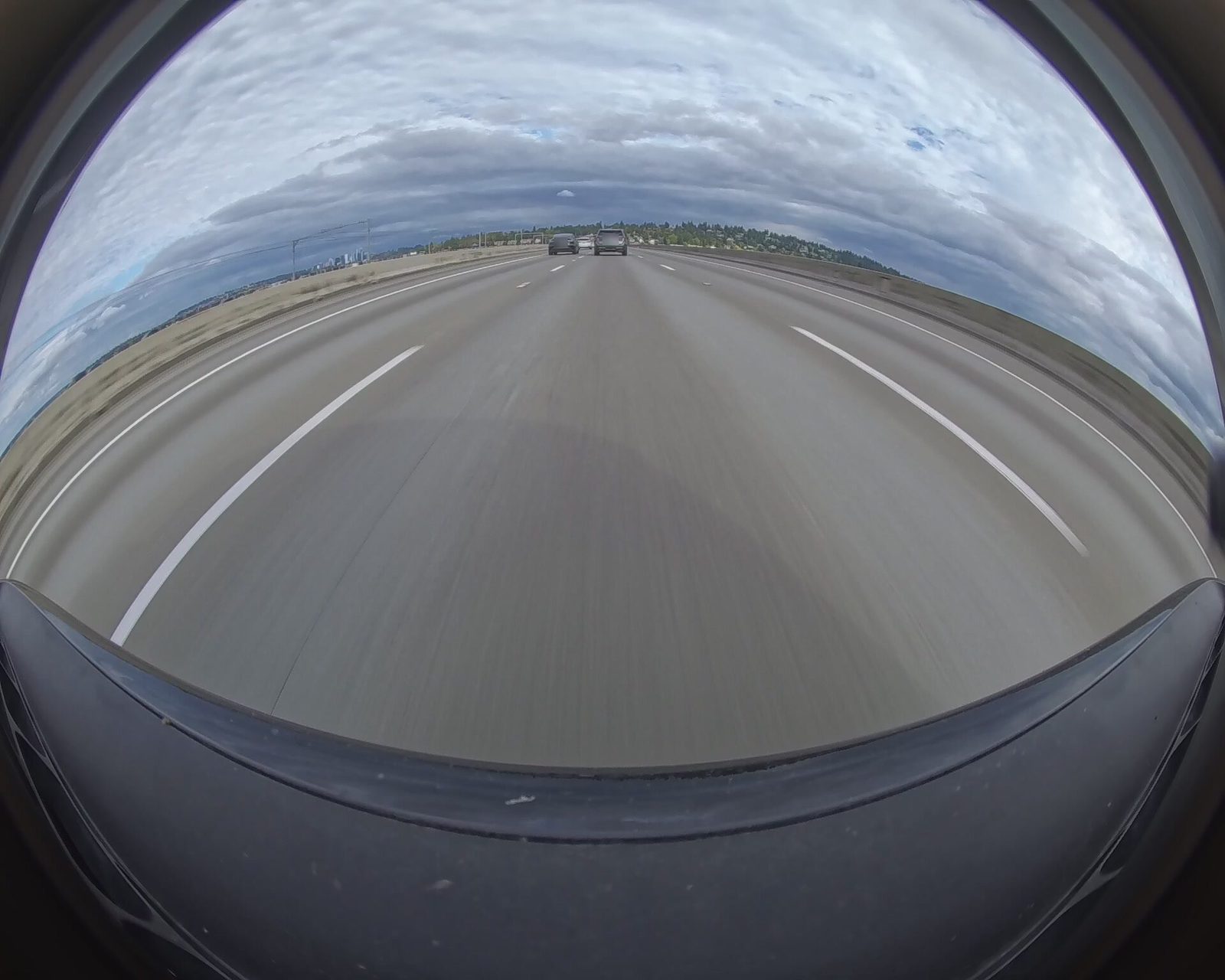 The front camera half a second into a segment that begins on the I-90 floating bridge under an overcast sky, with two cars ahead and a distant skyline low on the horizon.